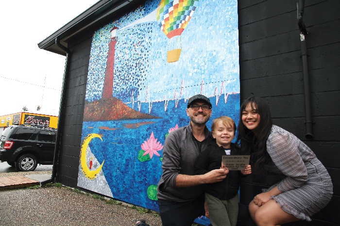 From left are Cork & Bone owner Jarrod Slugoski, his young son Oliver, who is depicted in the mural at bottom left sitting on the moon, and artist Jhade Acuna. 